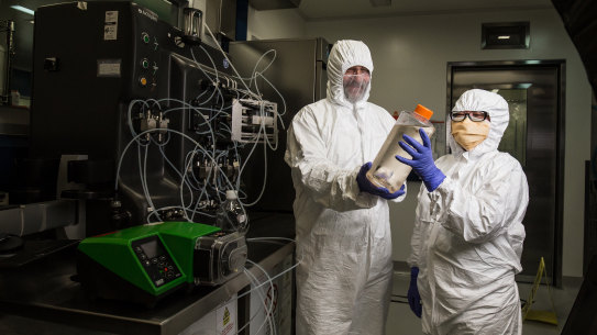 Professor George Lovrecz and Mylinh La at CSIRO's vaccine manufacturing plant in Clayton. They hold a bottle filled with cells that will be used to produce protein for the vaccine. Behind them is a machine that will eventually be used to purify the vaccine.