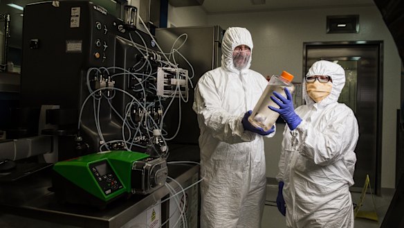 Professor George Lovrecz and Mylinh La at CSIRO's vaccine manufacturing plant in Clayton. They hold a bottle filled with cells that will be used to produce protein for the vaccine. Behind them is a machine that will eventually be used to purify the vaccine.