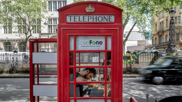A man works on repairing a cellphone in a LoveFone converted telephone booth in London.
