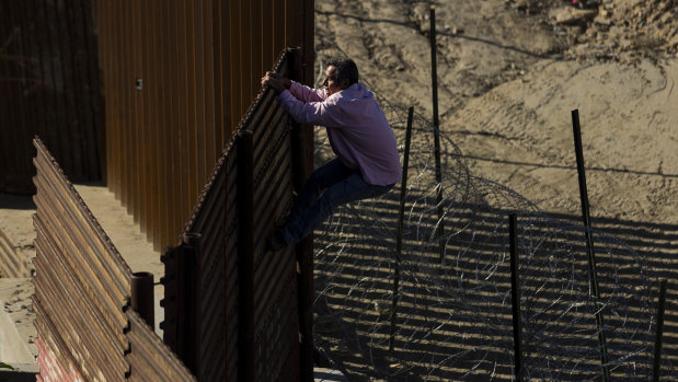 A migrant climbs the border fence to get from Tijuana, Mexico to San Diego in the US.