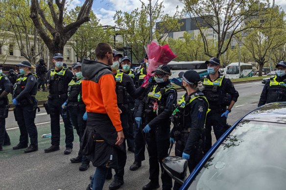 A man hands a police officer a bunch of flowers in Melbourne during protests that started outside the CFMEU headquarters in the CBD.