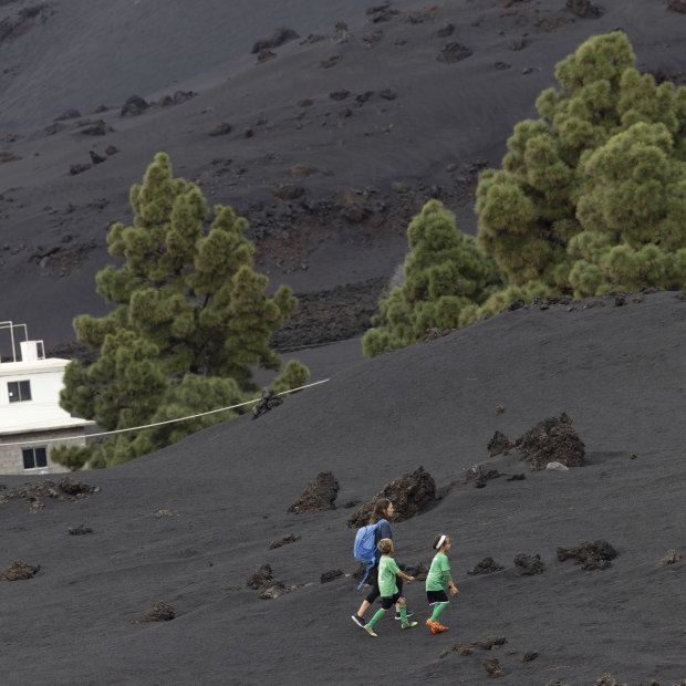 A family walks up a hill to a football field in the Las Manchas area of La Palma through an area entirely carpeted with volcanic ash.