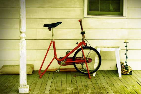 An exercise bike sits abandoned on a country porch. 