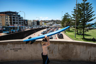 A child holding a surfboard walks past a queue at Bondi for COVID testing.