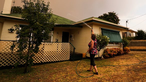 Bruthen resident Janine Pratt hoses down her home as burnt leaves fall on the property.