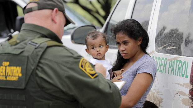 A mother migrating from Honduras holds her 1-year-old child as surrendering to U.S. Border Patrol agents after illegally crossing the border.