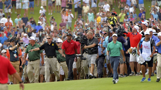 Swarm: The gallery engulfs Woods as he and Rory McIlroy walk up the 18th hole.