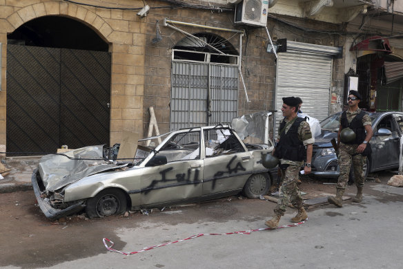 Soldiers walk past a car with graffiti in Arabic "Down with the military rule", near the site of the recent explosion in Beirut.