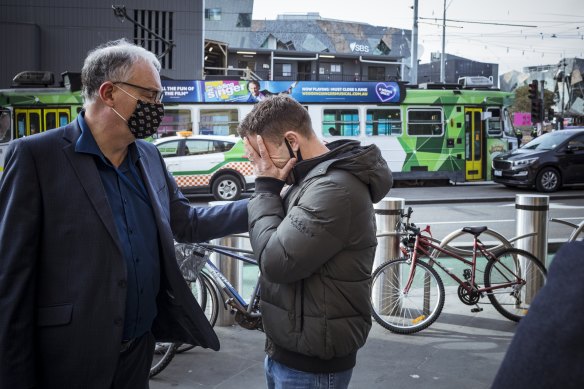 Small business owner Bill Panayotou is comforted after he became emotional talking about his business woes during lockdown outside Flinders Street Station.