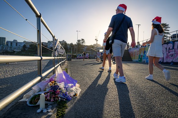 Beachgoers walk past flowers and candles left in remembrance of the victims of the Bondi mass shooting.