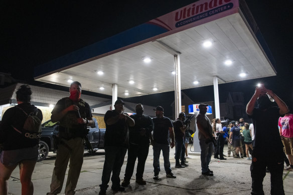 A group of armed individuals stand in front of Ultimate Convenience Centre in Kenosha during a protest over the shooting of Jacob Blake on Tuesday.