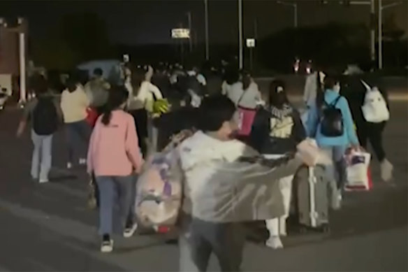 In this photo taken from video footage, people with suitcases and bags are seen leaving from a Foxconn compound in Zhengzhou.