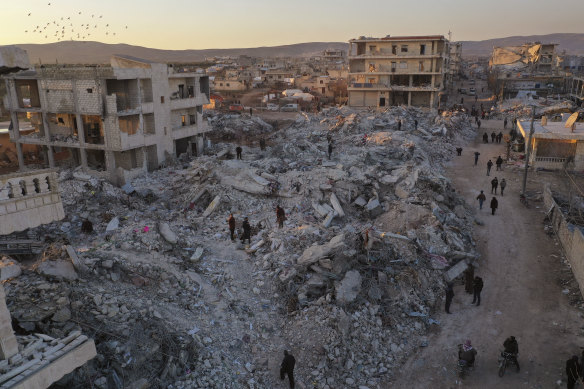 People walk past collapsed buildings following a devastating earthquake in the town of Jinderis, Aleppo province, Syria.