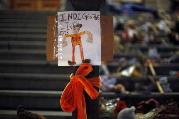 A sign is taped to a street lamp in front of a memorial to the victims of Canada’s residential school system. 