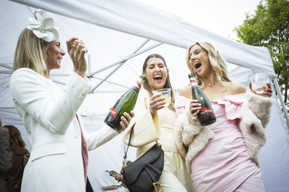 Caroline Knipe, Jasmine Ryan-Watson and Chelsea Matters crack open a champagne in the rain at the Melbourne Cup.