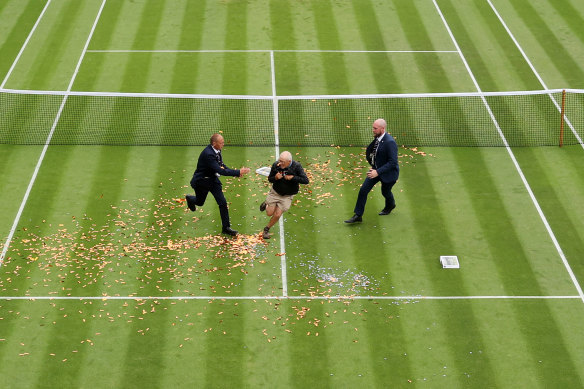 Security attempts to tackle a man who throw orange confetti and jigsaw pieces onto the court.