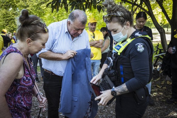 Craig Kelly shows a Victoria Police officer stains on his jacket after being egged in a Melbourne park on Friday.