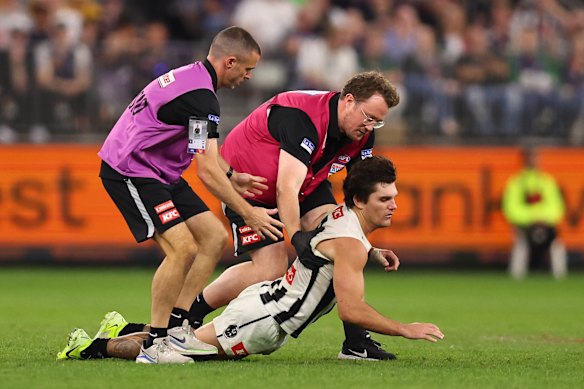 Lachie Schultz of the Magpies collapses in the hands of medical staff.