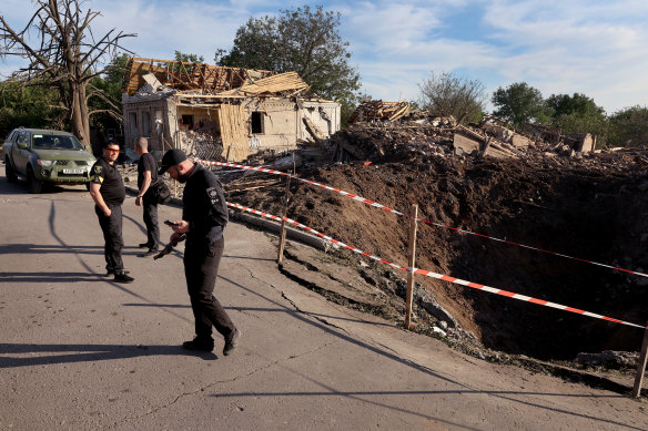 Police stand next to a crater left following a missile strike in Druzhkivka, Ukraine.