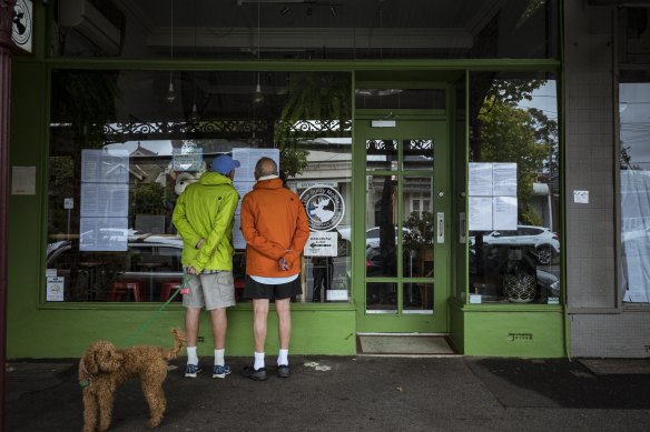 Local residents read a message about the coronavirus and the cafe's dealings with DHHS on the window of The Guilty Moose cafe in Albert Park.