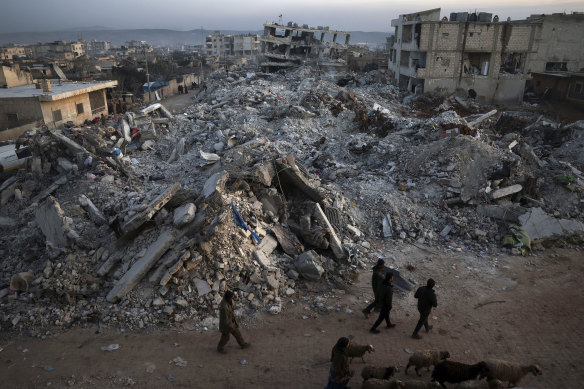 People walk past collapsed buildings following a devastating earthquake in the town of Jinderis, Aleppo province, Syria.