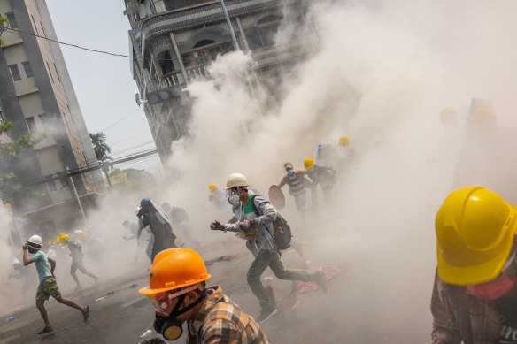 Anti-coup protesters run after riot police fire tear gas in Yangon.