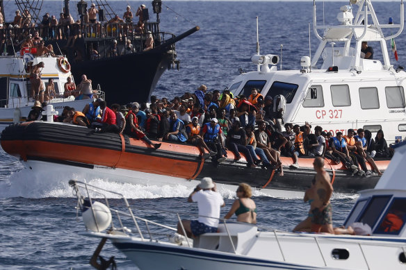 An Italian coast guard boat carries migrants as tourists on a boat watch near the Sicilian island of Lampedusa, in southern Italy.