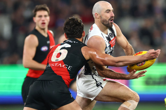 Steele Sidebottom of the Magpies handballs whilst being tackled by Jye Caldwell of the Bombers.