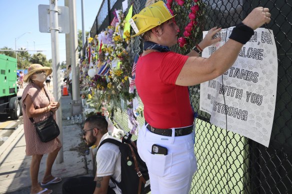 Local resident Alison Kairuz pins her hand-made sign to the fence in support of families and friends who lost love ones at a memorial site for victims.