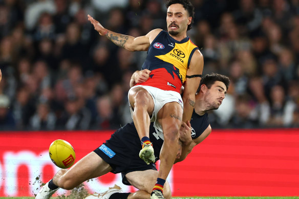 Izak Rankine of the Crows kicks whilst being tackled by George Hewett of the Blues.