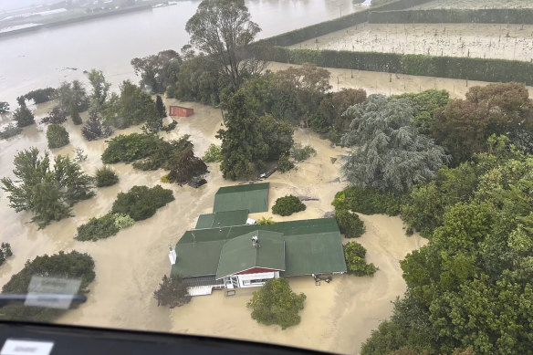 People stand on a rooftop of a home waiting to be winched to safety by helicopter in the Esk Valley, near Napier, New Zealand, in the aftermath of Cyclone Gabrielle.