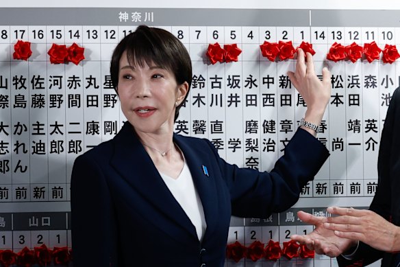 Sanae Takaichi places a red rose on the name of one of her winning candidates at the LDP party’s headquarters. 