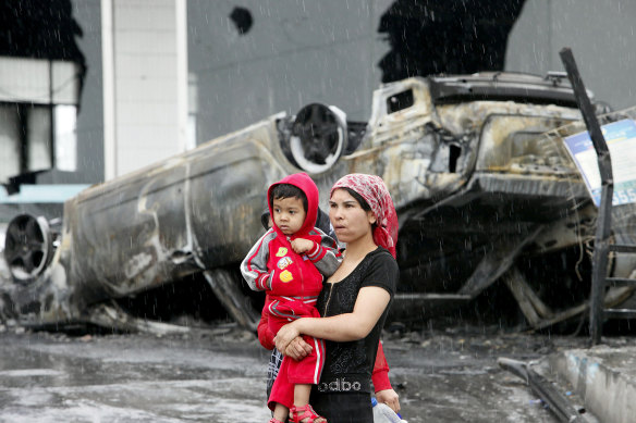 A Uighur woman and a child walk past a burnt car at a destroyed dealership  following riots in Urumqi, western China's Xinjiang province in 2009. Analysts say the riots set in motion the harsh security measures now in place.