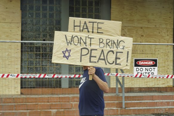 A man holding a sign reading “Hate won’t Bring Peace” walks in front of the Adass Israel on Saturday.