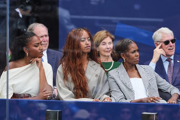 Sasha, Malia and Michelle Obama listen to Barack Obama speak, with George and Laura Bush and Bill Clinton behind them.