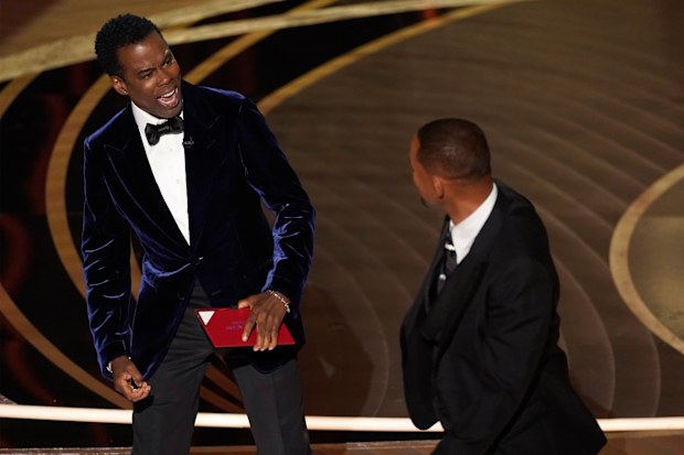 presenter Chris Rock, left, reacts after being hit on stage by Will Smith while presenting the award for best documentary feature at the Oscars on Sunday, March 27, 2022, at the Dolby Theatre in Los Angeles. (AP Photo/Chris Pizzello)