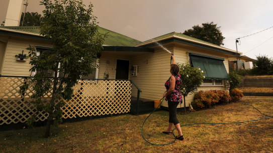 Resident of Bruthen in East Gippsland Janine Pratt hoses down her home on Monday as burning leaves fall on the roof.