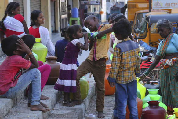 An Indian boy helps a girl to drink water as others wait to collect potable water from a public tap in a poor area of Hyderabad, India.