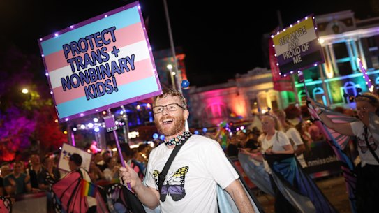 A parade participant at the Sydney Gay and Lesbian Mardi Gras Festival 2025 holding up a sign saying: “Protect trans + nonbinary kids!”