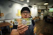 Philip Leong, from TWS Gai Wong chicken restaurant, holds a counterfeit $100 note at his restaurant in North Melbourne.
