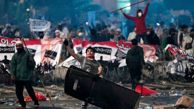 A supporter of Indonesian presidential candidate Prabowo Subianto throws a rock at riot police.