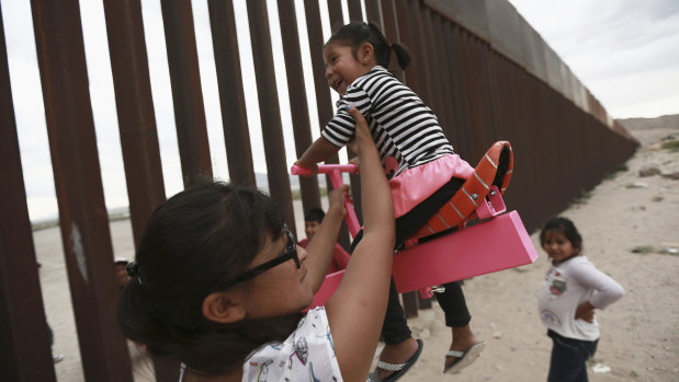 A woman helps her girls play on a seesaw installed between the border fence that divides Mexico from the United States in Ciudad de Juarez, Mexico.