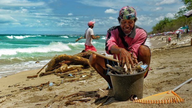 Wayan Wetra cleans the beach space in front of his stall at Kuta Beach.