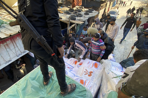 Palestinians unload wheat sacks from a humanitarian aid truck into a grocery store under guard by Hamas fighters in Rafah, Gaza Strip.