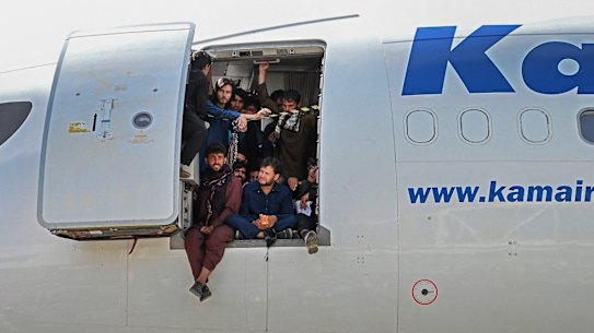 Afghan people climb up on a plane and sit by the door as they wait at the Kabul airport, the morning after thousands of people ran onto the tarmac trying to flee the Taliban. 