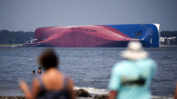 Visitors to driftwood beach watch a Moran tugboat near the stern of the vessel Golden Ray as it lies on its side. The ship overturned in September last year.