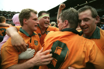 Michael Lynagh (left) is hugged by Phil Kearns (taped head) as they embrace Australian captain Nick Farr-Jones as they celebrate victory at the final whistle. Winger Bob Egerton is on the right.