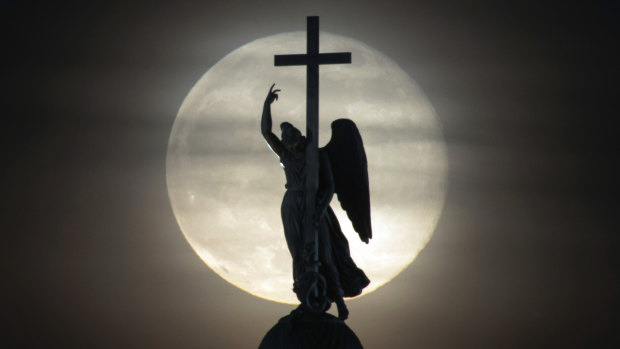 A statue of an angel fixed atop the Alexander Column at the Palace Square is silhouetted on the rising full moon in St. Petersburg, Russia.