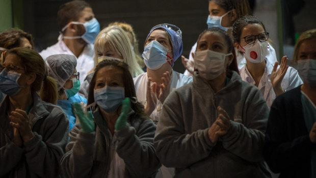Health workers react as people applaud from their houses in support of the medical staff that are working on the COVID-19 virus outbreak at the main gate of the Hospital Clinic in Barcelona, Spain.