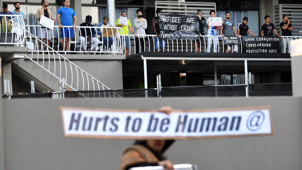 A refugee supporter walks by holding a sign as asylum seekers who are being held in detention at an inner city motel are seen protesting in Brisbane.